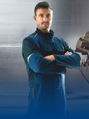 Metalworker wears work clothes and posts with arms folded.
